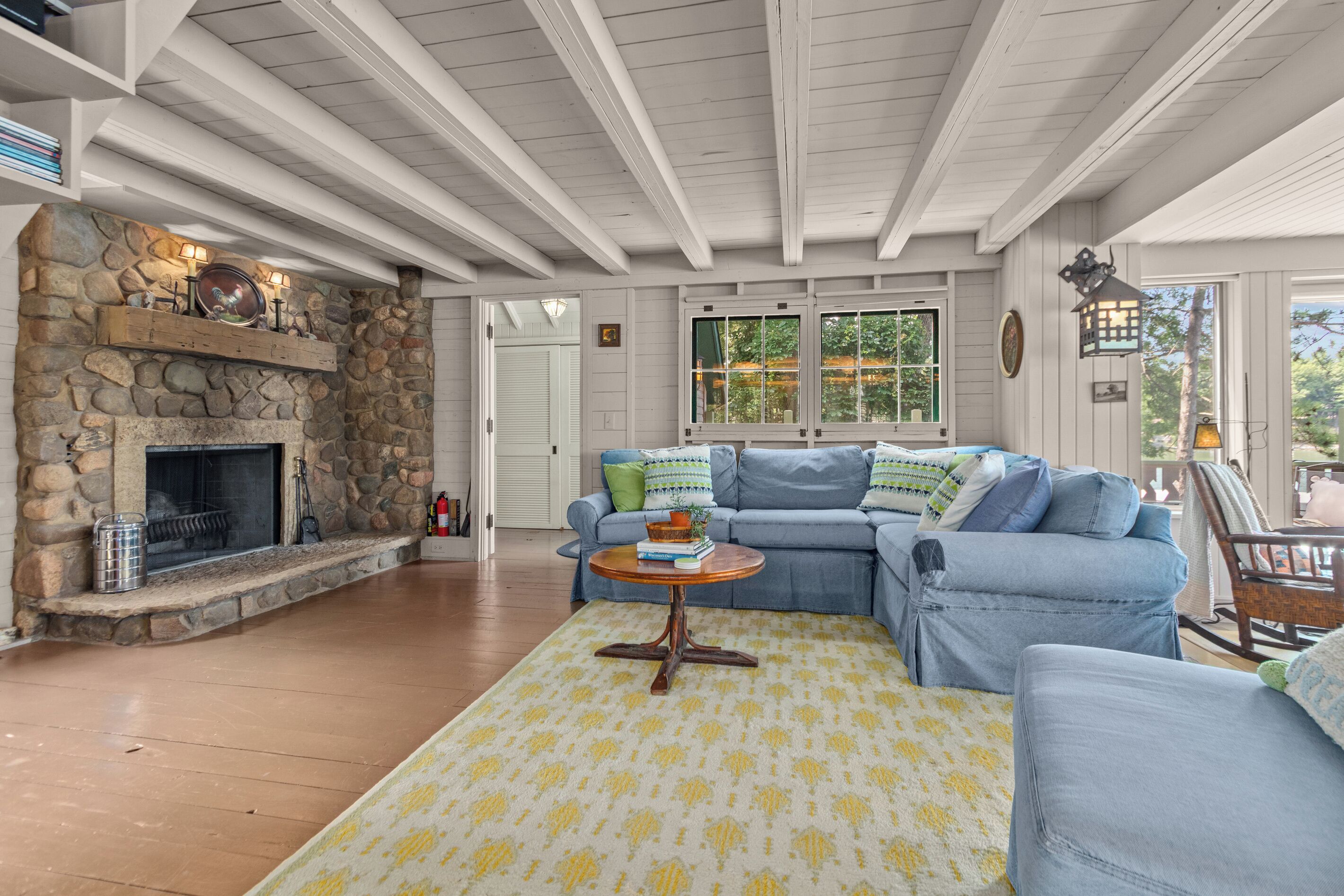 A living room with a stone fireplace, a blue sofa, and a wooden ceiling.