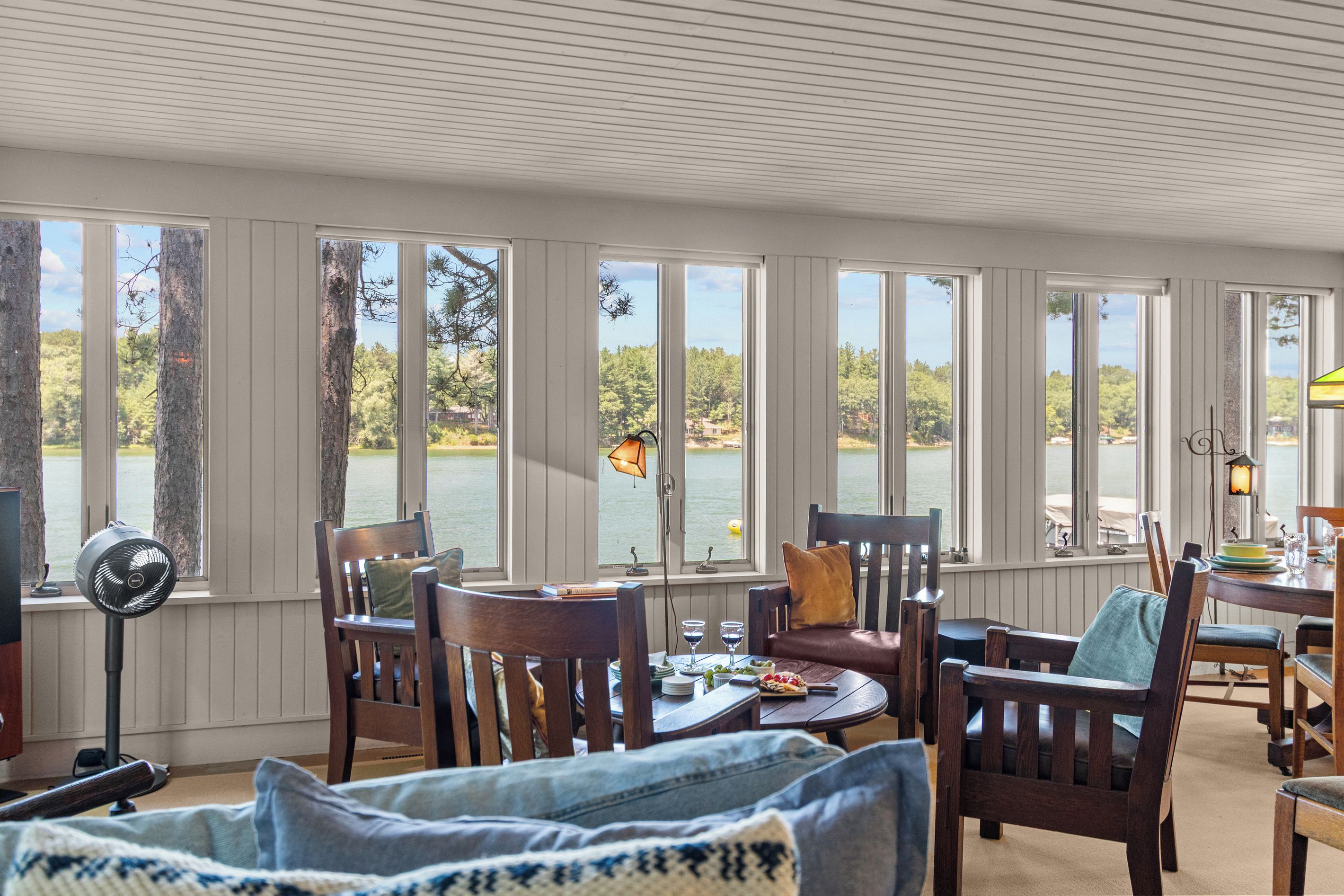 A room with a large window overlooking a body of water, wooden furniture, and a fan.