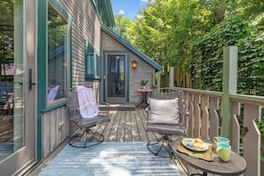 A wooden deck with outdoor seating, a table with food, and a view of a house with a door and windows.