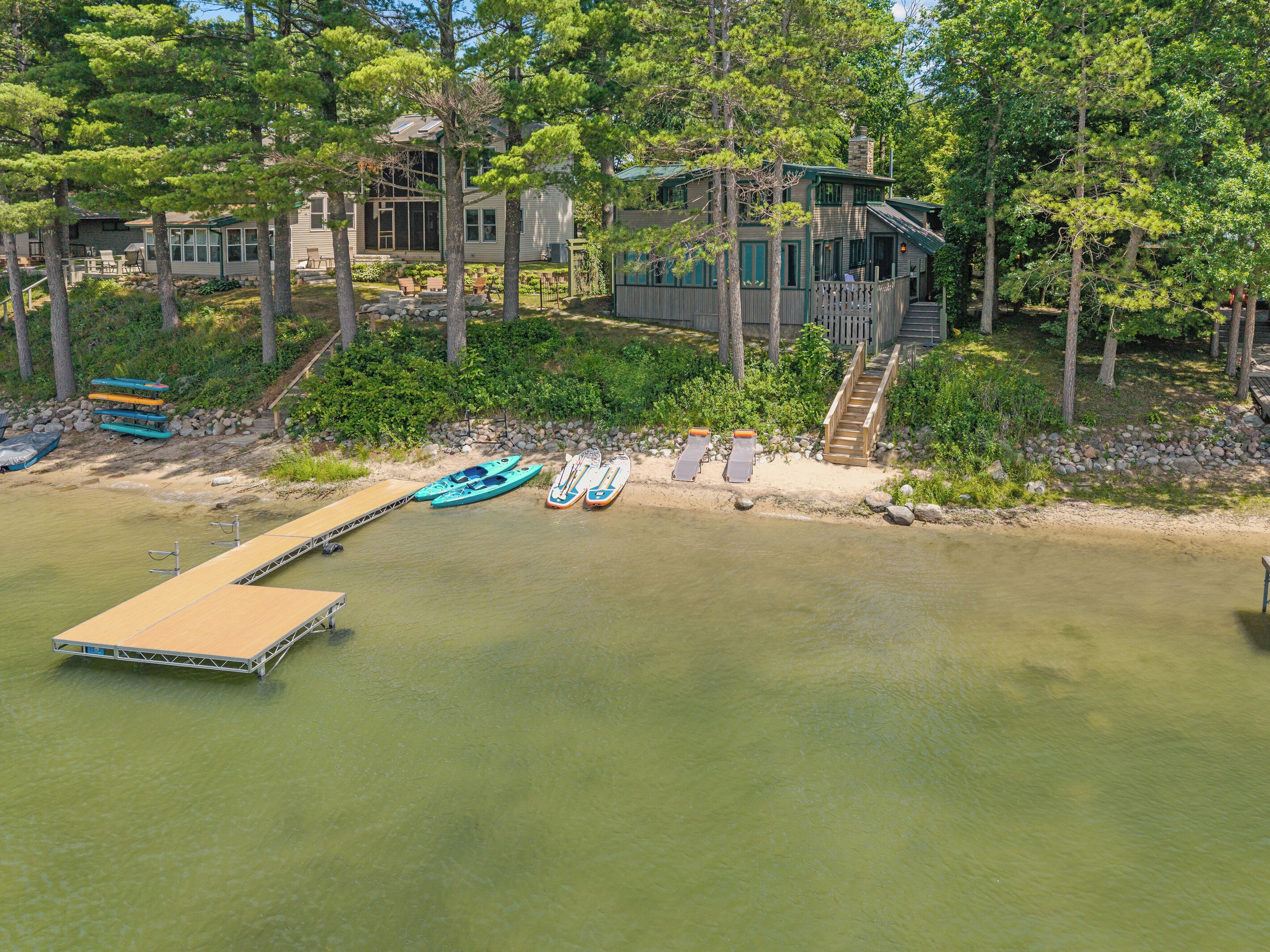 Una propiedad frente al lago con muelle, kayaks y una escalera de madera que lleva a una casa.