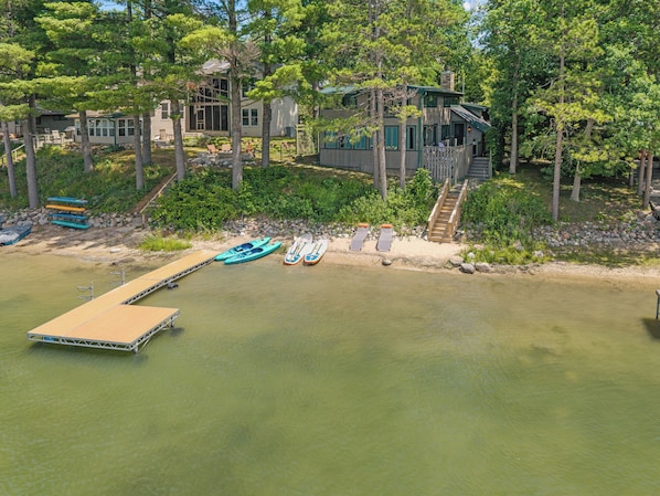 A lakeside property with a dock, kayaks, and a wooden staircase leading to a house.