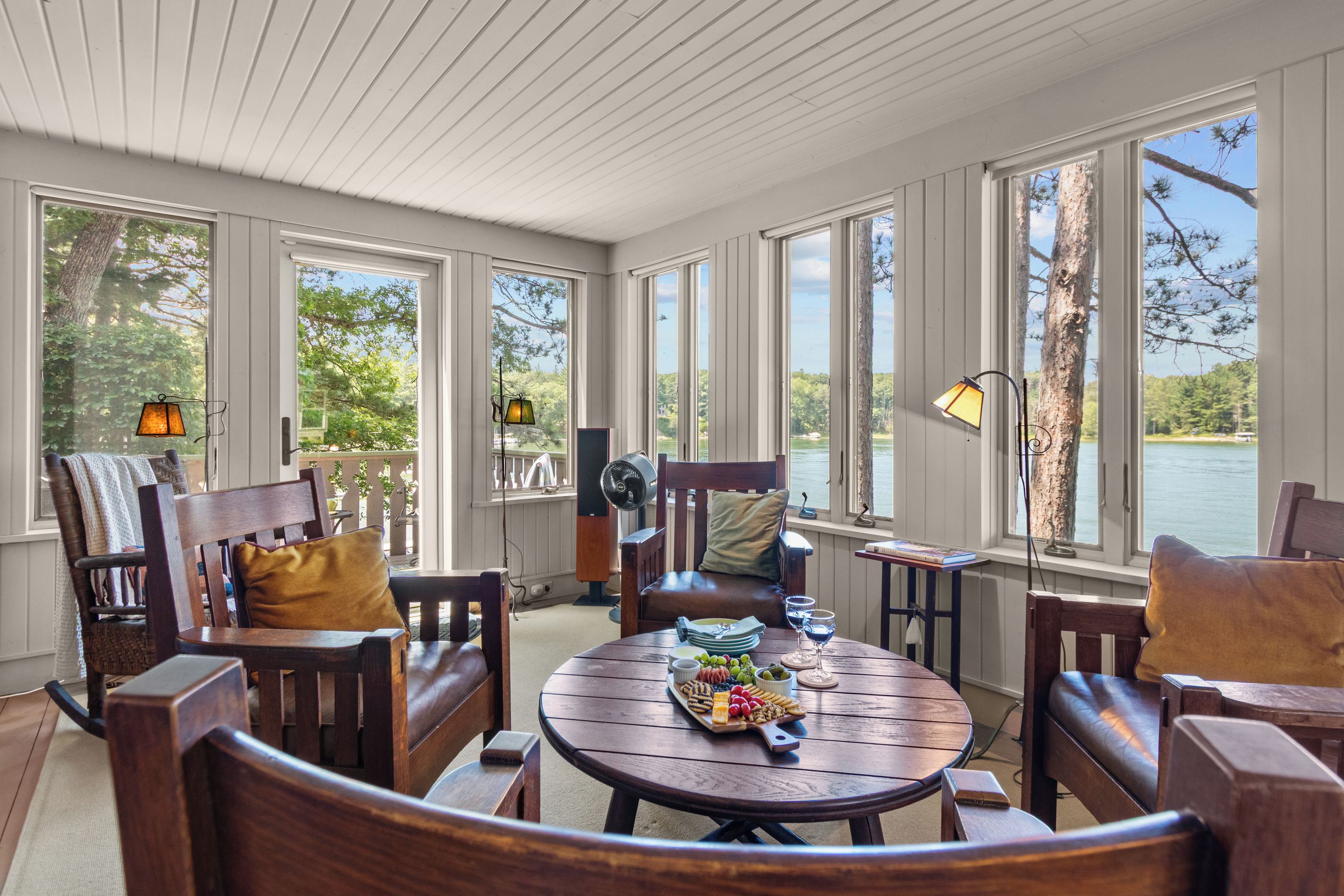 A sunlit room with large windows, wooden furniture, and a table set with snacks.