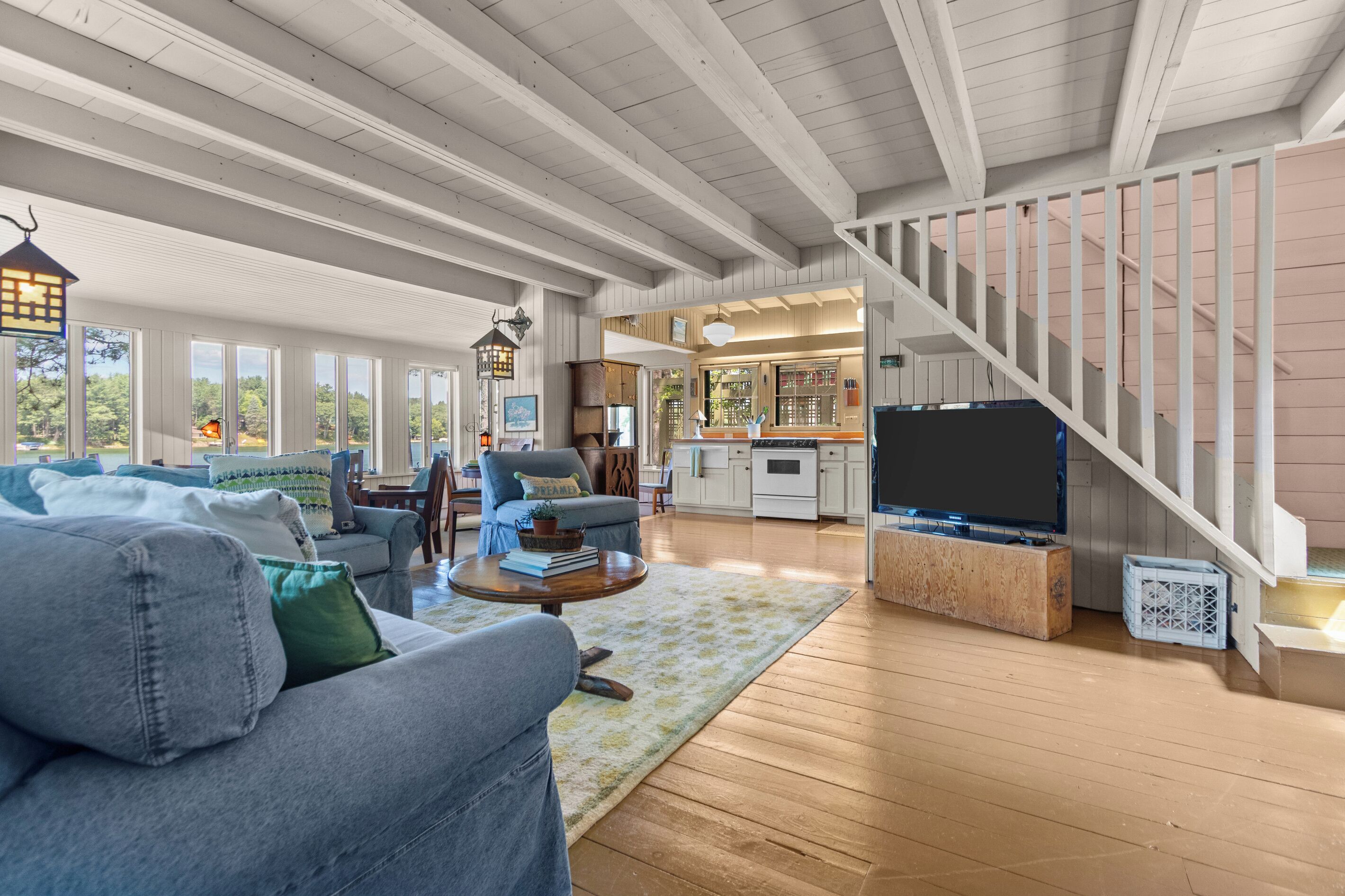 A spacious living room with a high ceiling, a staircase, and a kitchen area.