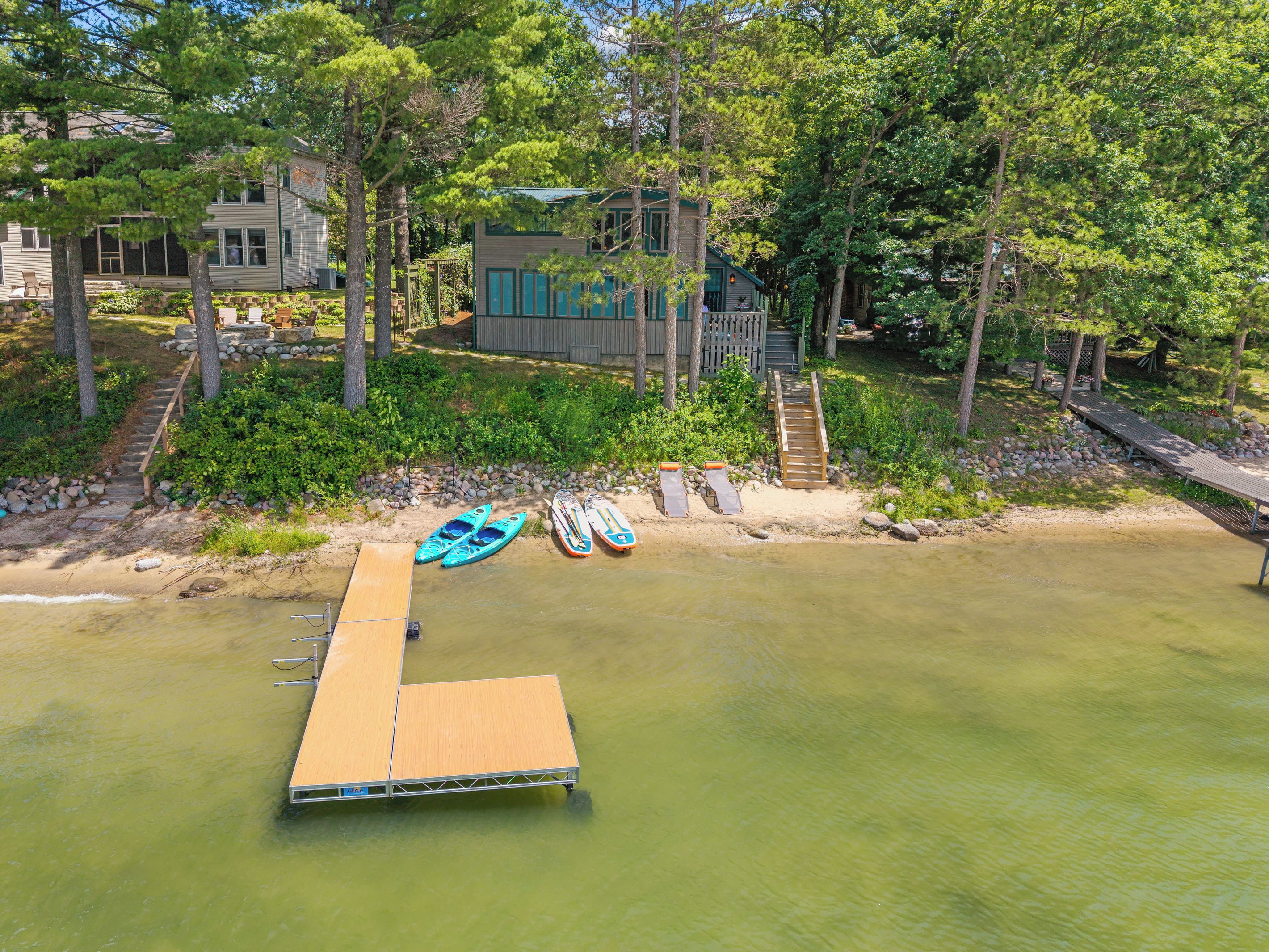 A lakeside property with a dock, kayaks, and a house surrounded by trees.
