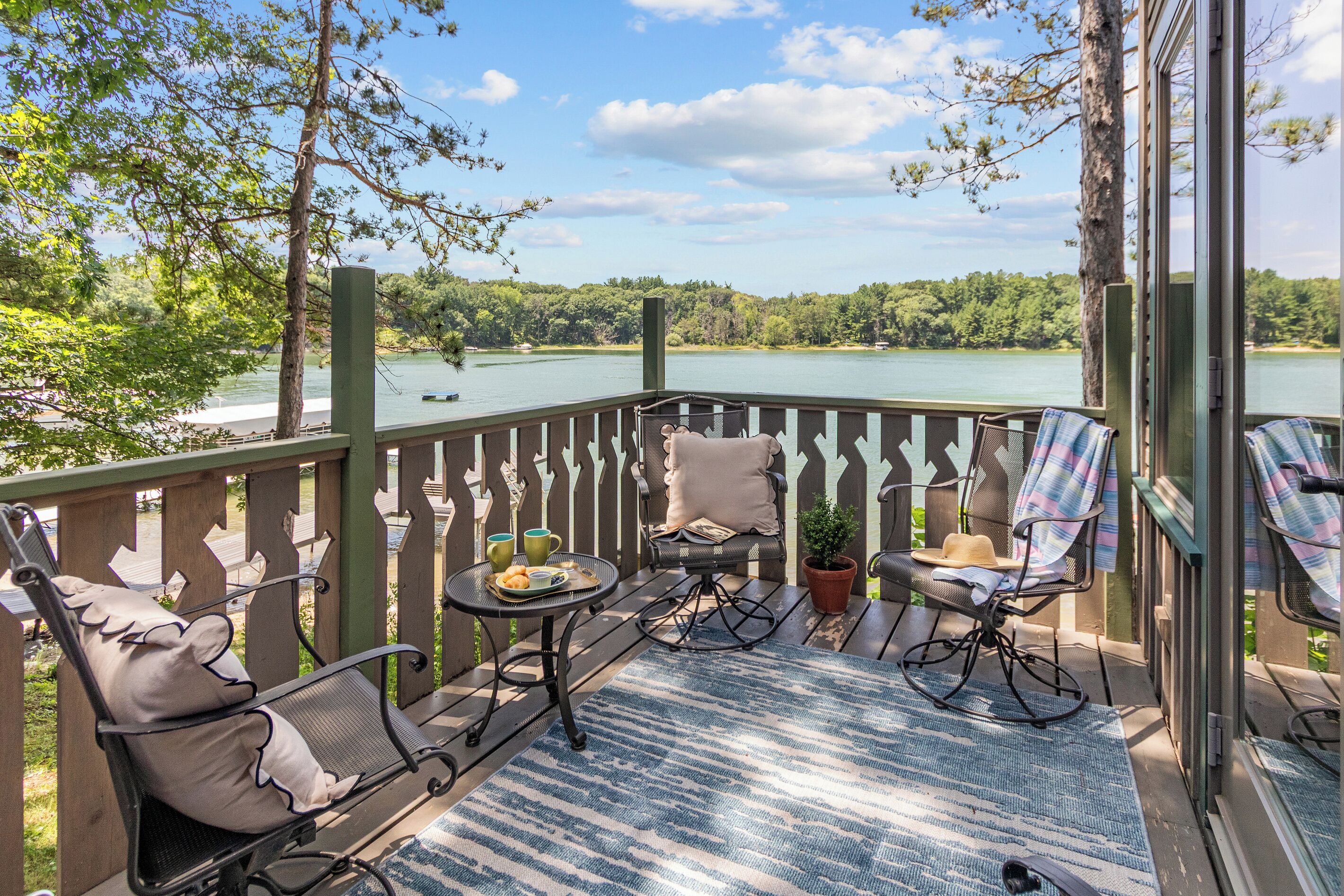 A deck with outdoor furniture, a view of a lake, and a forested landscape.