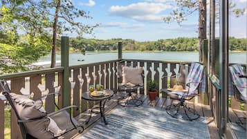 A deck with outdoor furniture, a view of a lake, and a forested landscape.