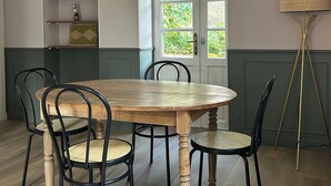 Een eetkamer met een houten tafel, zwarte stoelen, een hanglamp en een deur met uitzicht op groen.