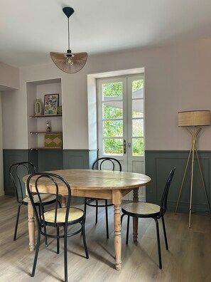 A dining room with a wooden table, black chairs, a hanging light fixture, and a door with a view of greenery. - Juliette's House (Ussac)