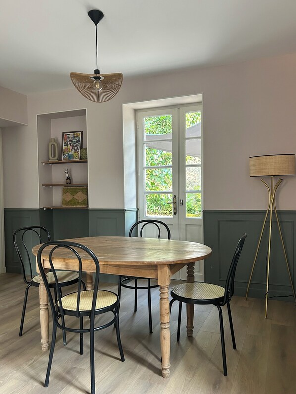 A dining room with a wooden table, black chairs, a hanging light fixture, and a door with a view of greenery. - Juliette's House (Ussac)