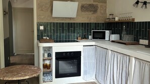 Een kleine keuken met een inbouwoven, een magnetron en een eethoekje met een ronde tafel.