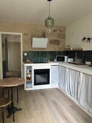 A compact kitchen with a built-in oven, a microwave, and a small dining area with a round table. - Juliette's House (Ussac)