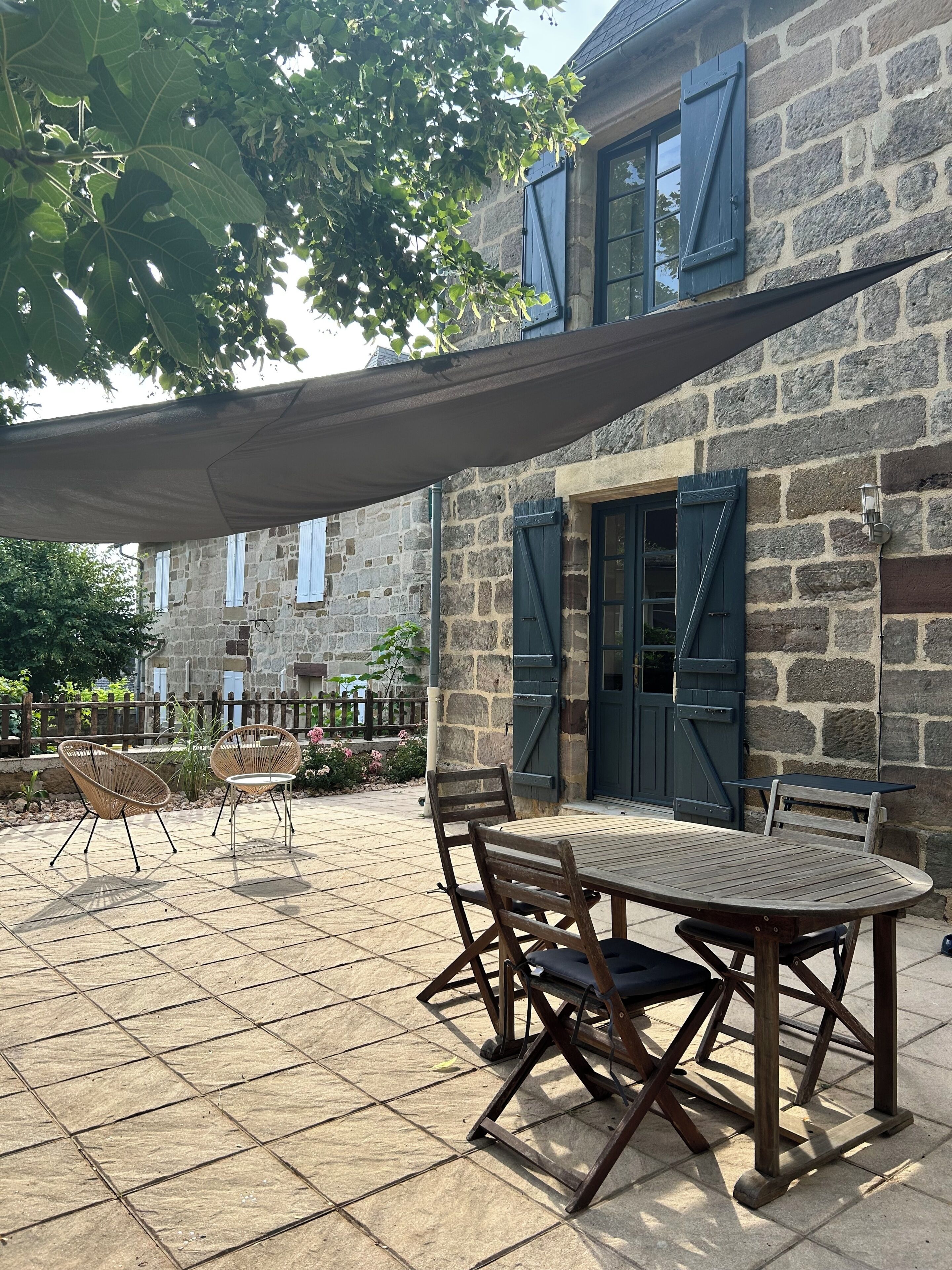 A stone building with a patio area featuring a table and chairs, a pergola, and a stone fence.