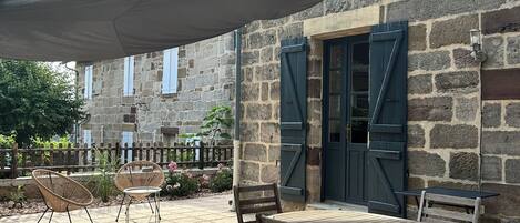 A stone building with a patio area featuring a table and chairs, a pergola, and a stone fence.