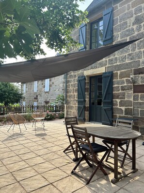 A stone building with a patio area featuring a table and chairs, a pergola, and a stone fence.