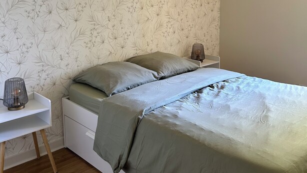 Een slaapkamer met een bed, nachtkastjes, een lamp en een plafondventilator.