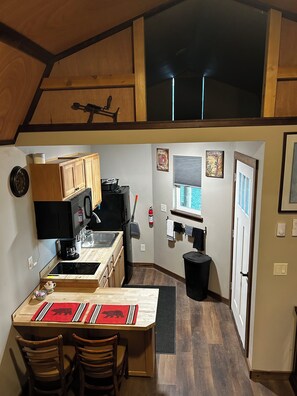 A compact kitchen with wooden cabinets, a black refrigerator, a stove, and a dining area with two chairs.