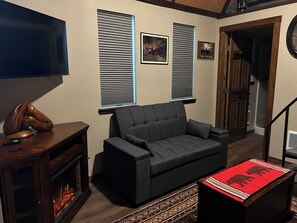 A living room with a sofa, a fireplace, a television, and two windows with blinds.