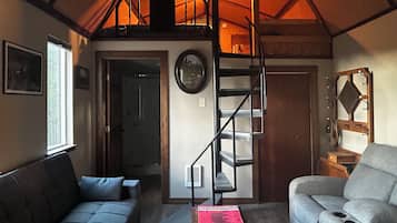 Un intérieur chaleureux avec un lit en mezzanine, un escalier, un canapé et un fauteuil.