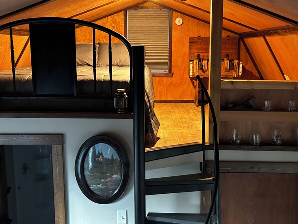 A cozy interior with a bunk bed, a small table with glasses, and a window with a view of a forest.