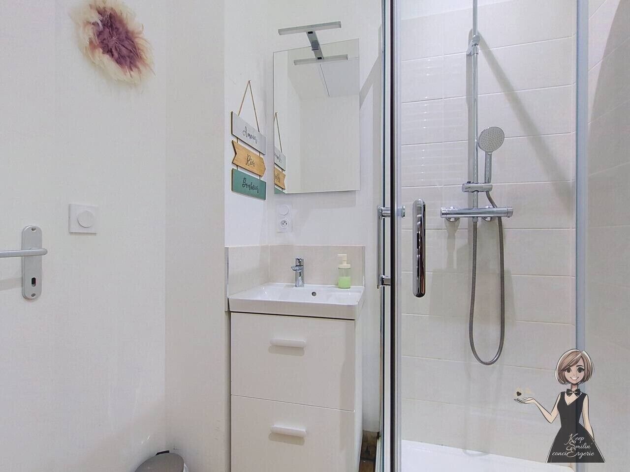 A bathroom with a glass shower enclosure, a sink with a mirror above it, and a small decorative item on the wall.