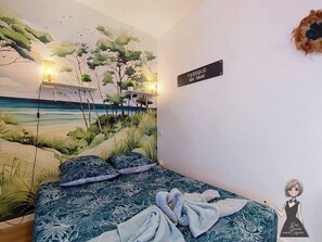 Ein Schlafzimmer mit Strandwandgemälde, einem Bett mit gemusterten Betttextilien und einem Wandschild.