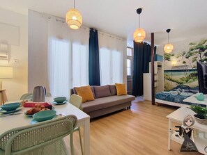 Ein modernes Wohnzimmer mit einer Couch, einem Esstisch und einem Bett mit Wandgestaltung im Strandstil.
