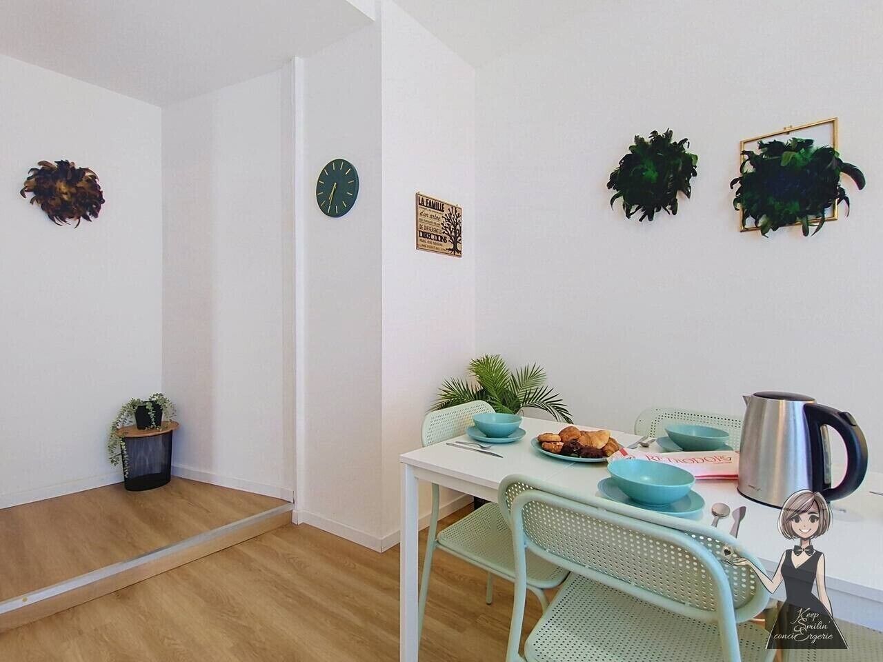 A dining area with a table set for two, a clock, and decorative wall art.
