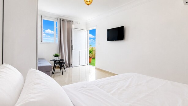 Une chambre d’hôtel avec un lit, un téléviseur fixé au mur, une petite table avec une plante et une vue sur l’extérieur par une fenêtre.