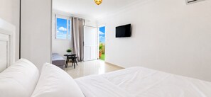 A hotel room with a bed, a TV mounted on the wall, a small table with a plant, and a view of the outdoors through a window. - Penthouse  Appartment close to Agadir Beach (Agadir)