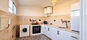 Eine kleine Küche mit Waschmaschine, Backofen und Spüle, versehen mit einem modernen Wasserhahn.