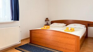 Ein Einzelbett mit Holz-Kopfteil, ein Nachttisch mit Lampe und ein zusammenrolltes Handtuch auf dem Bett.