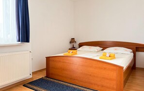 Ein Einzelbett mit Holz-Kopfteil, ein Nachttisch mit Lampe und ein zusammenrolltes Handtuch auf dem Bett.