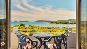 Ein Balkon mit Tisch und Stühlen mit Blick auf eine Küstenlandschaft mit Hügeln und einem Gewässer.
