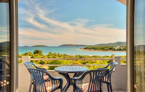 Ein Balkon mit Tisch und Stühlen mit Blick auf eine Küstenlandschaft mit Hügeln und einem Gewässer.