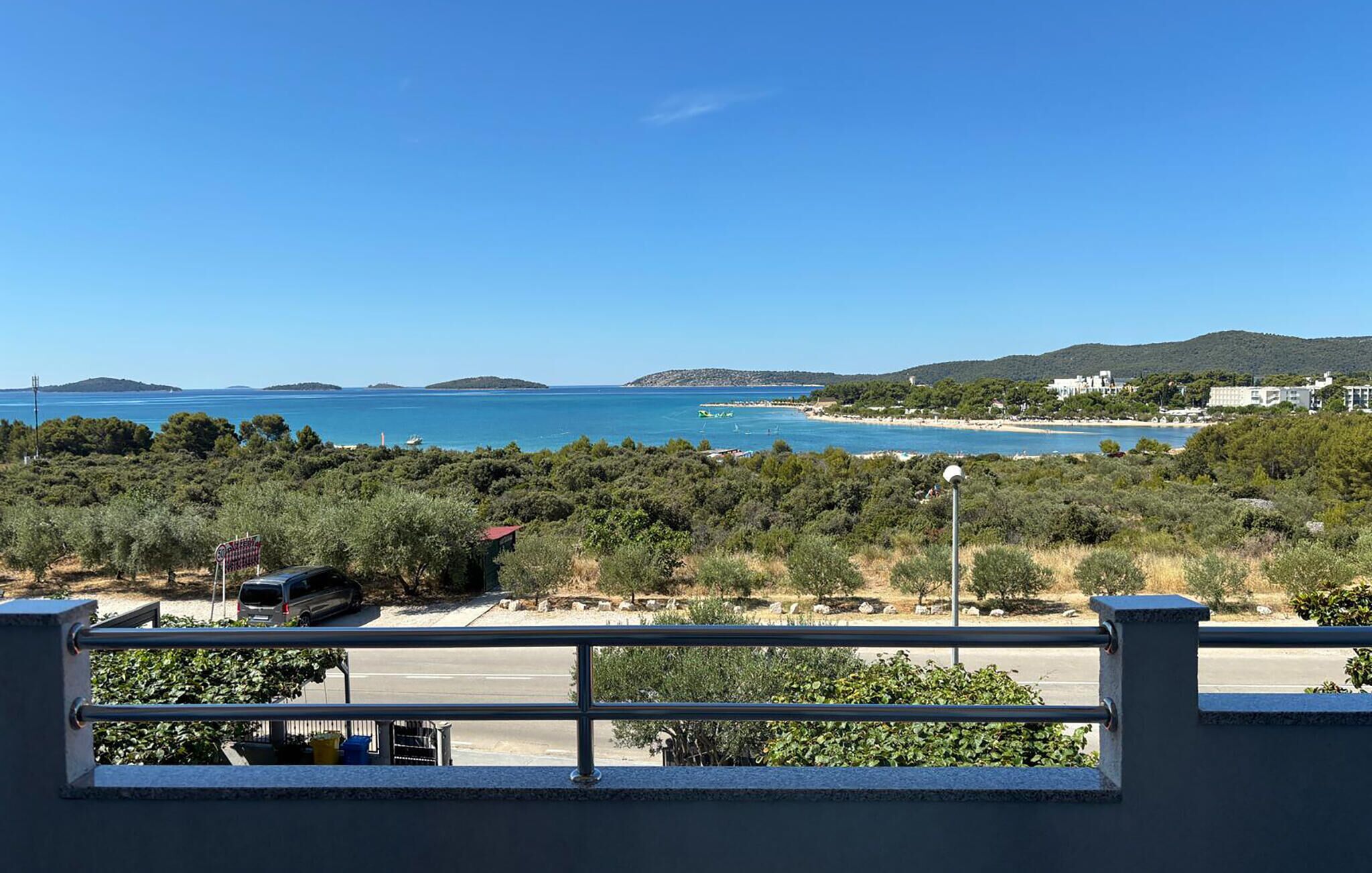 A coastal view with a clear sky, a beach, and a road leading to a building.