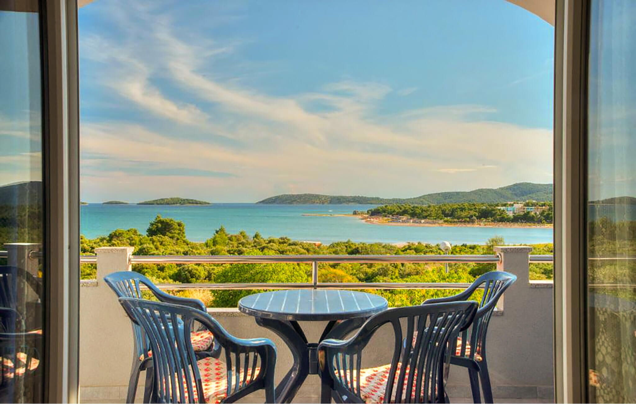 Ein Balkon mit zwei Stühlen und einem Tisch, der auf eine Küstenlandschaft mit Hügeln und einem Wasserlauf blickt.