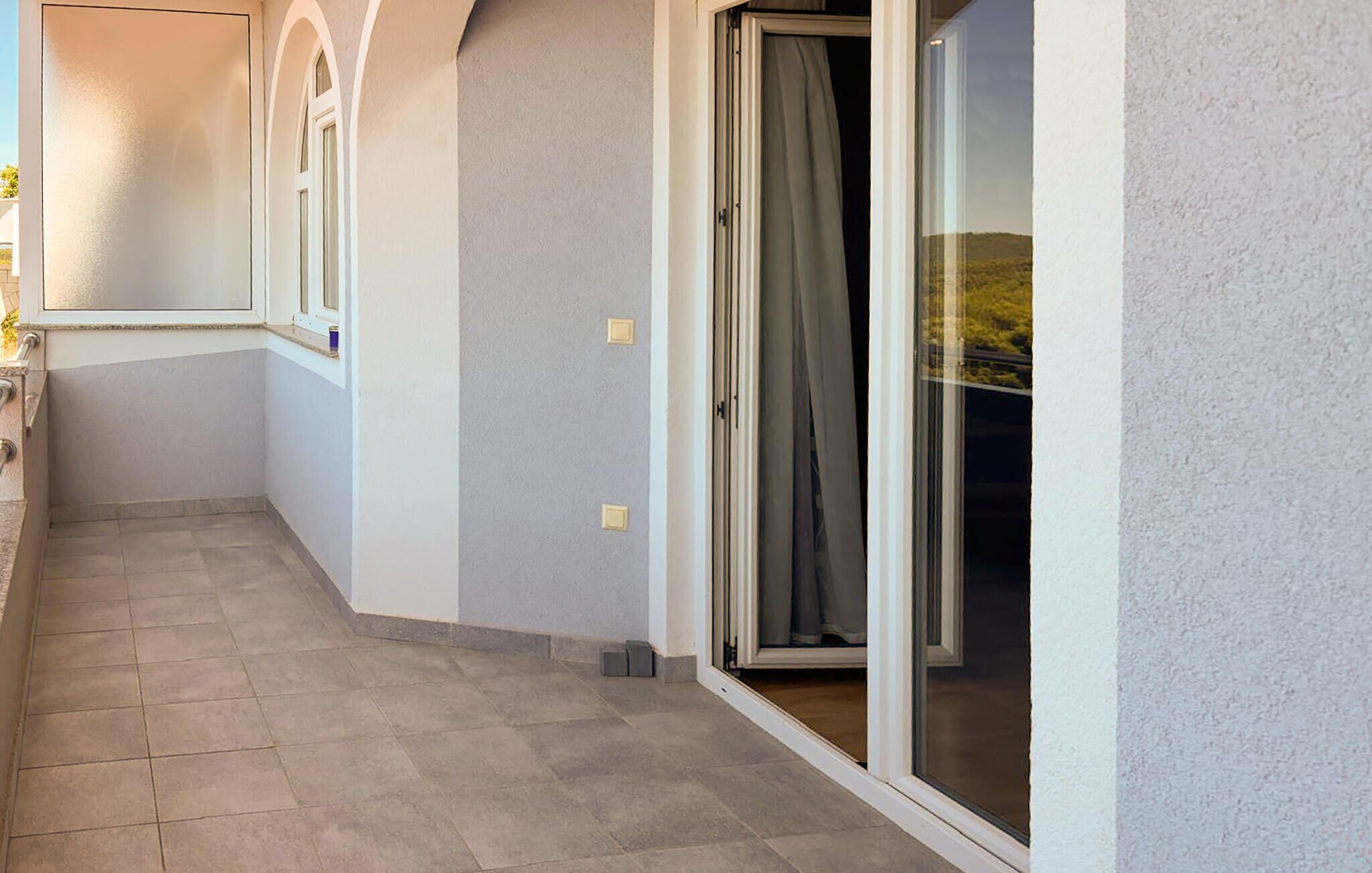 A corridor with a tiled floor, a door with a curtain, and a window with a view of greenery.