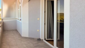 Ein Korridor mit Fliesenboden, einer Tür mit Vorhang und einem Fenster mit Blick auf Grünflächen.