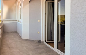Un pasillo con suelo de baldosas, una puerta con cortina y una ventana con vista a la vegetación.