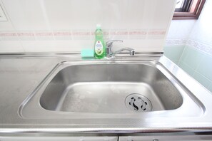 A stainless steel kitchen sink with a green bottle of dish soap and a sponge. - Shinjuku 7-chome | Spacious Accommodations for 6 Guests · Wi-Fi Available · Perfect for Sightseeing and Long-Term Stays (新宿区新宿)