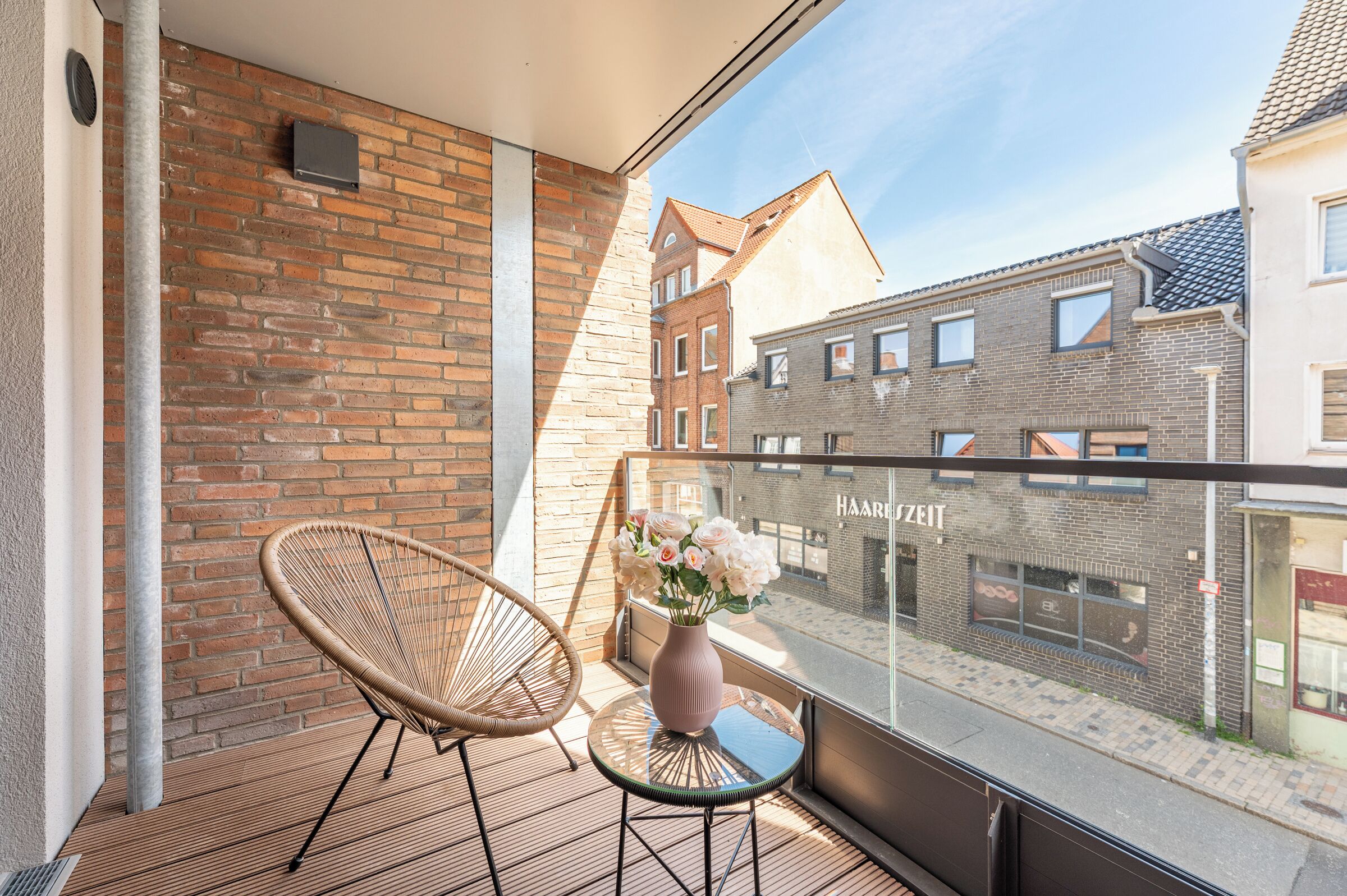 Ein Balkon mit Korbstuhl, einem kleinen Tisch mit Blumenvase und Blick auf die Nachgebäud
