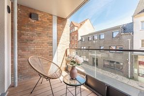 A balcony with a wicker chair, a small table with a vase of flowers, and a view of adjacent buildings. - NordicNeustadt: A Scandinavian-modern apartment in the heart of Husum (Husum)