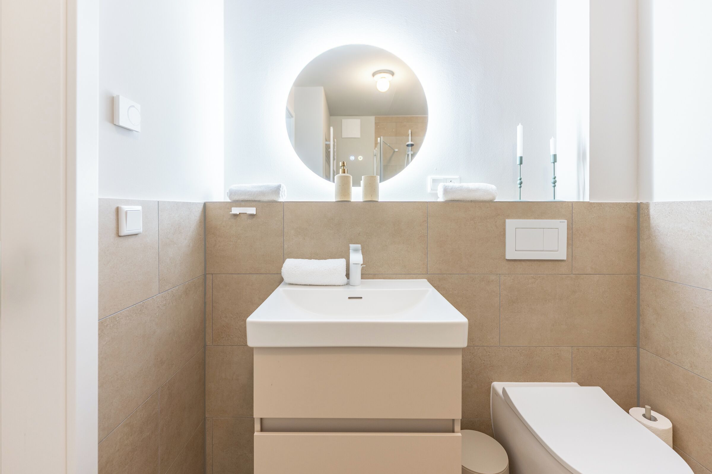 Une salle de bain moderne avec un miroir rond, un lavabo et des toilettes.