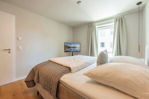 A bedroom with a bed, a television, a window with curtains, and a door. - NordicNeustadt: A Scandinavian-modern apartment in the heart of Husum (Husum)