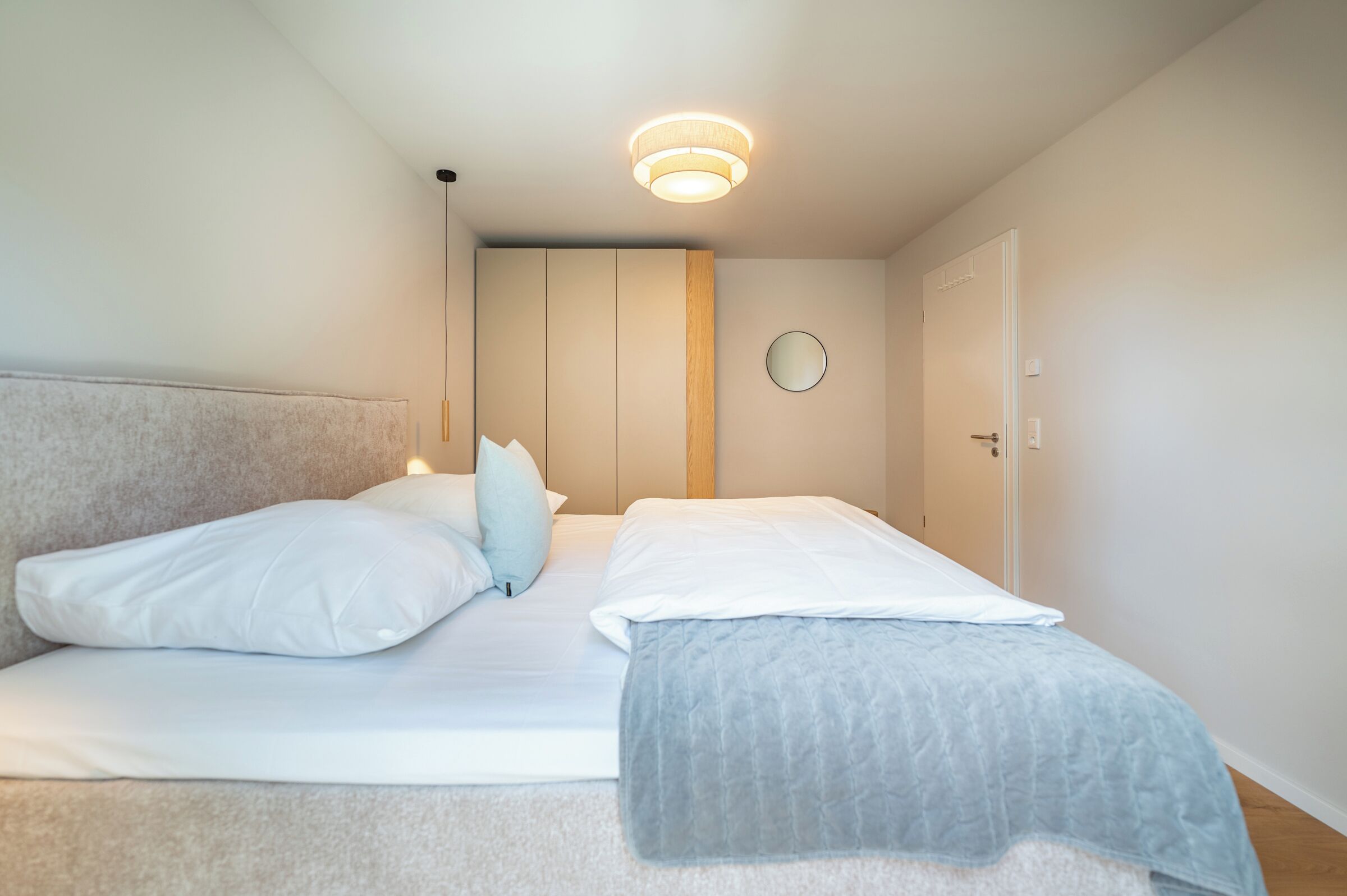 Een slaapkamer met een bed, kussens, een nachtkastje, een spiegel aan de muur en een deur.