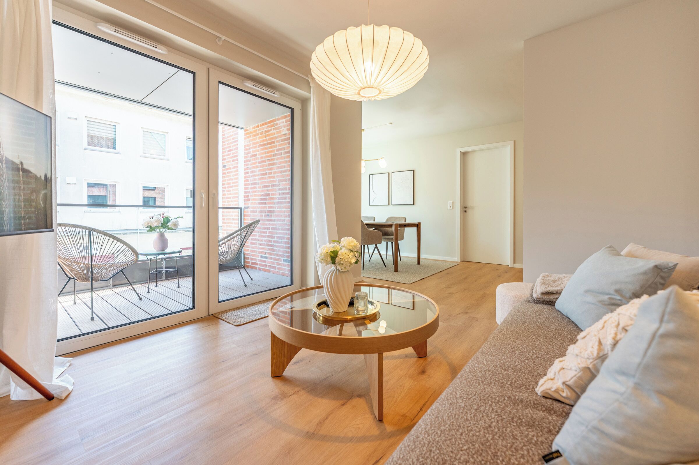 A modern living room with a glass coffee table, a sofa, and a dining area with chairs.