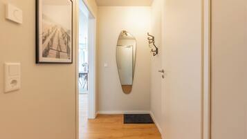 A hallway with a wooden floor, a door with a mirror, and a framed picture on the wall.