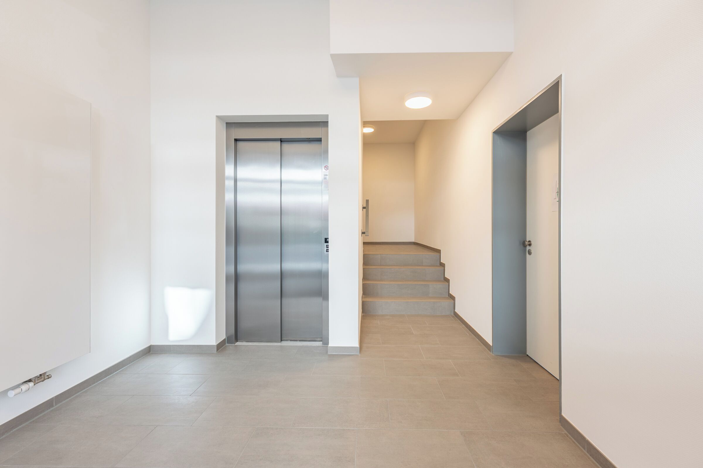 Ein Flur mit einem geschlossenen Aufzug und einer Treppe, die zu einer anderen Etage führt.