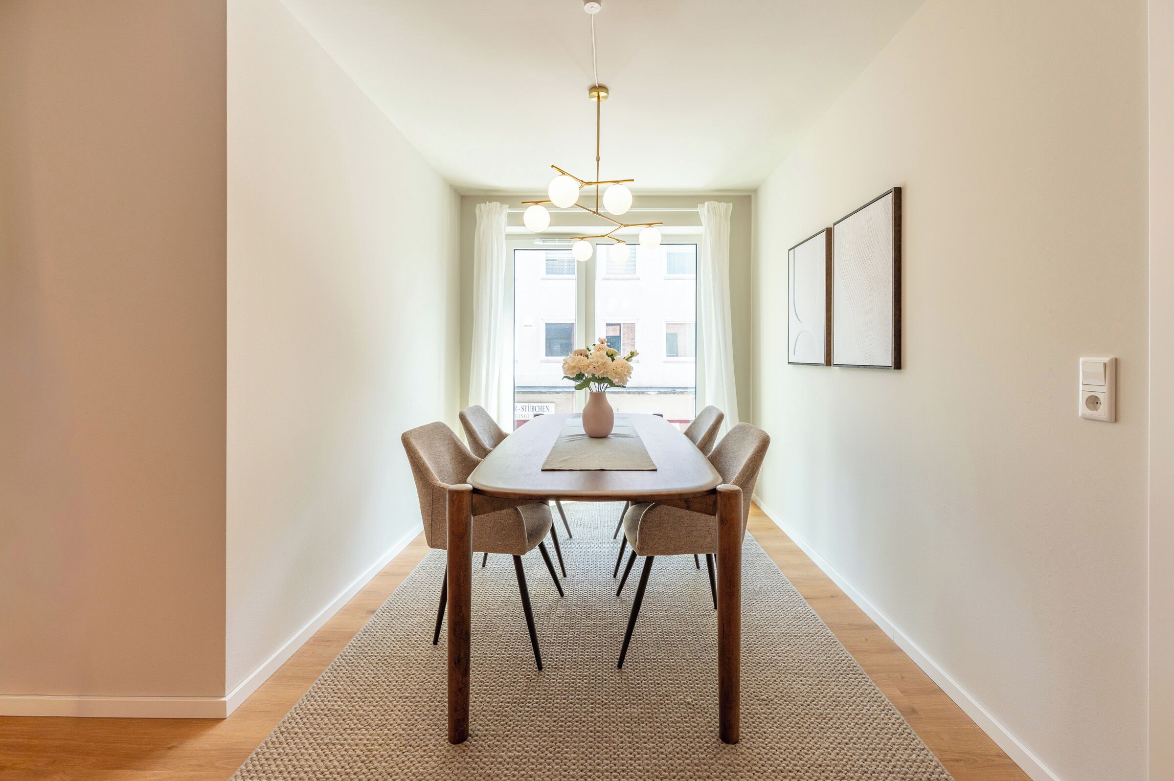 A dining area with a table, chairs, a vase with flowers, and a hanging light fixture.