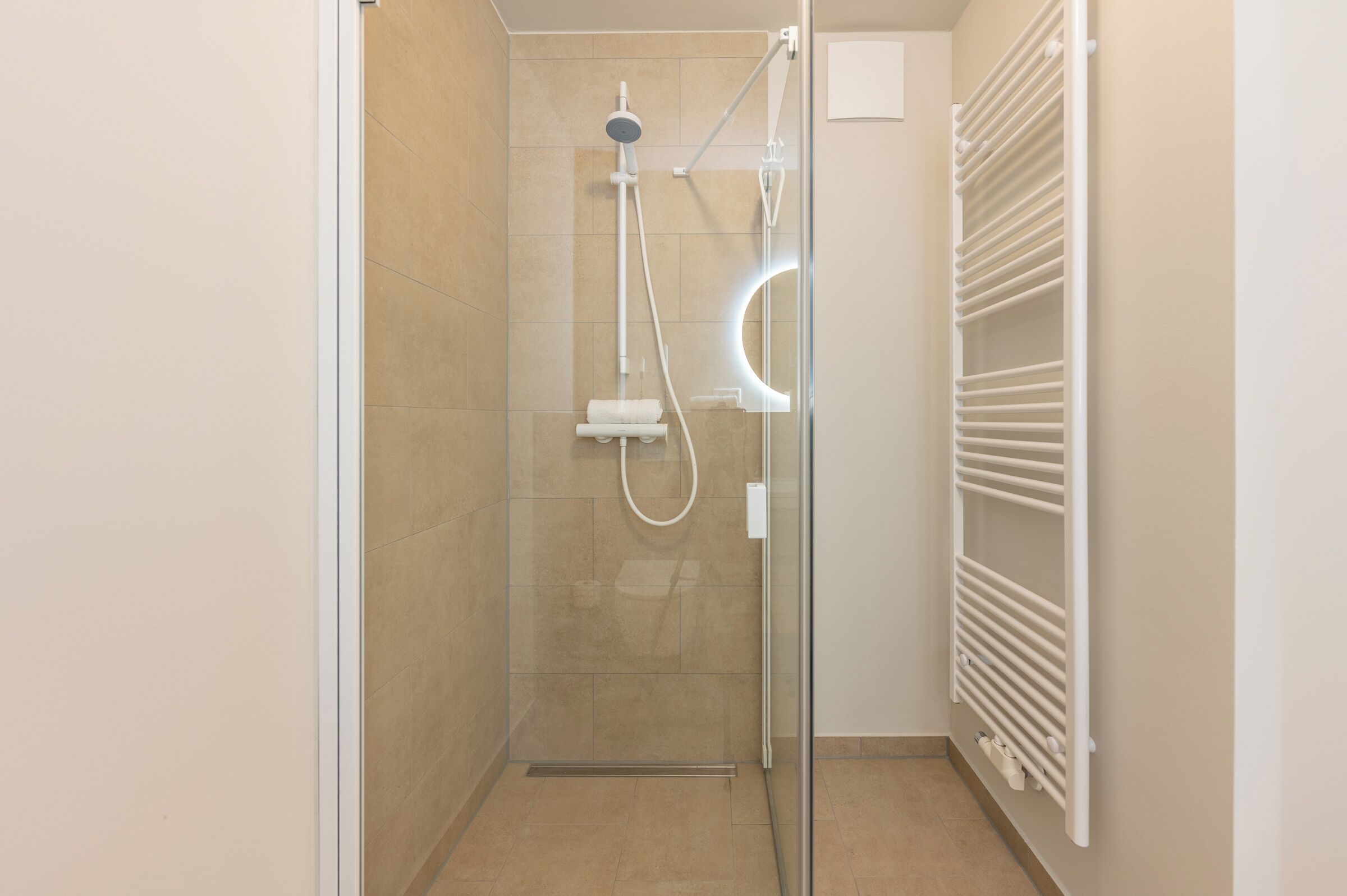 Eine Dusche mit Glastür, ein weißes Handtuch und ein an der Wand montierter Handtuchwärmer.